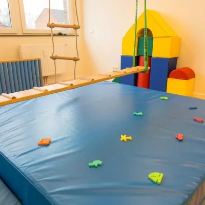 Bewegungsraum mit großer blauer Weichbodenmatte, Hängebrücke und bunten Schaumstoffbausteinen