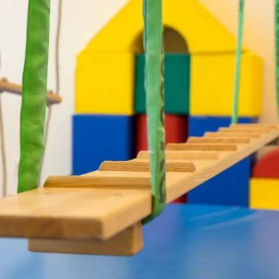 Hölzerne Hängebrücke an grünen Gurten vor bunten Bausteinen