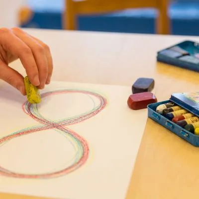 Hand malt mit Wachsmalblöcken eine liegende Acht auf Papier