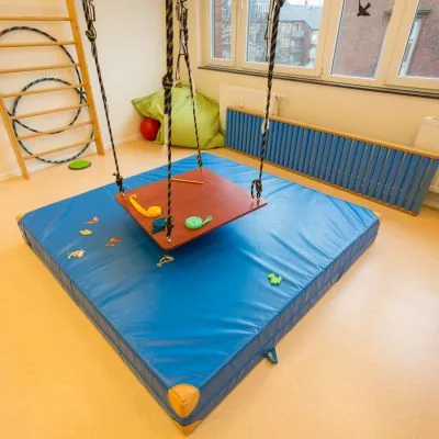 Therapieschaukel über einer Weichbodenmatte, im Hintergrund eine Sprossenwand